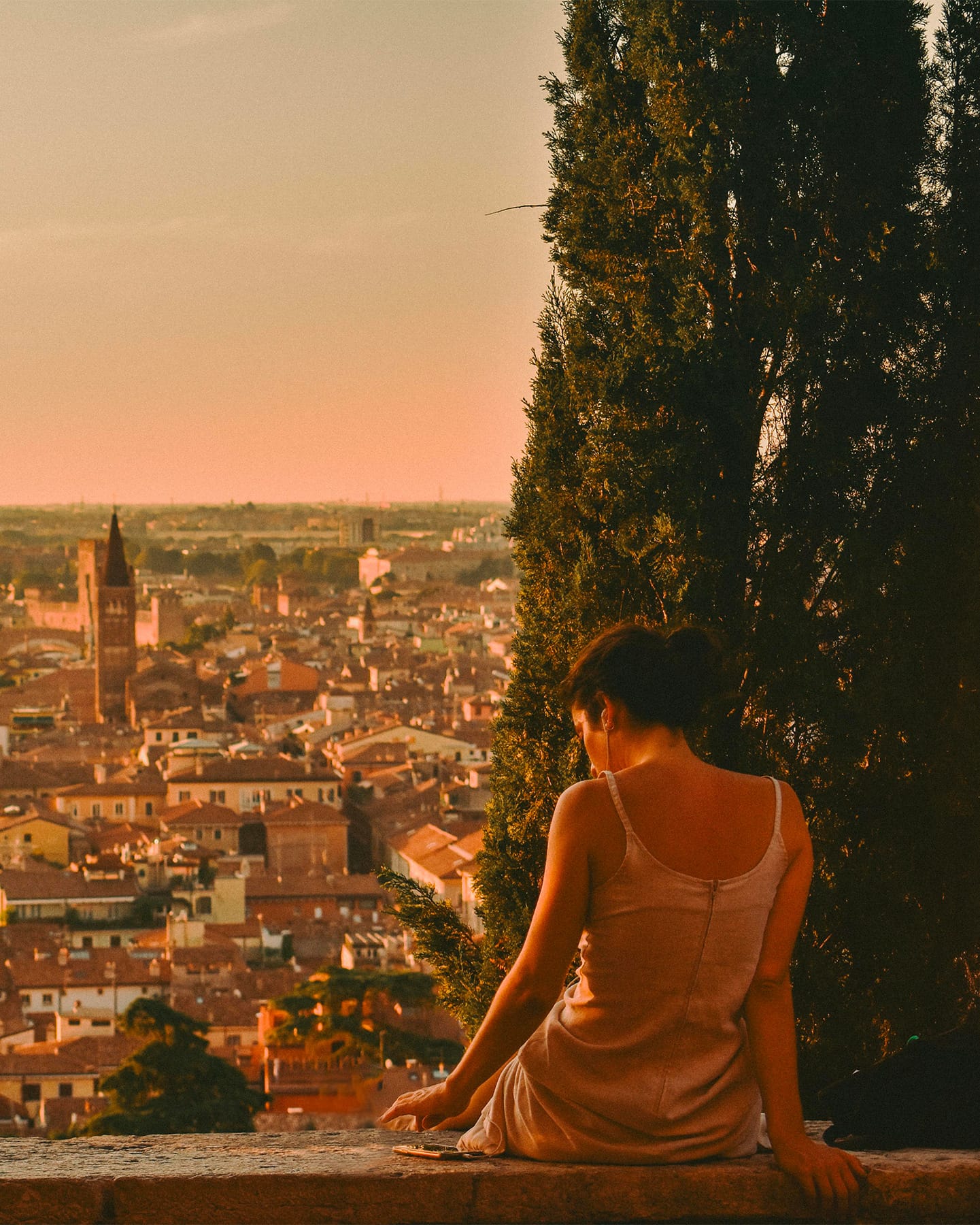Woman sitting and looking at a city at sunset